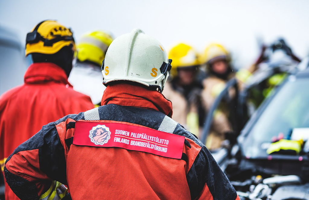 Kypäräpäinen kouluttaja selin kameraan. Selässä lukee teksti: Suomen Palopäällystöliitto.