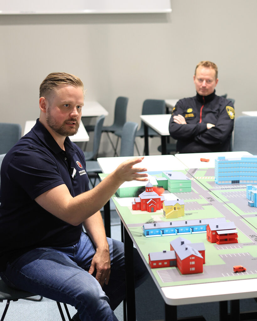 Ihmisiä pelastustoiminnan johtamisen simulaattoripöydän ääressä.